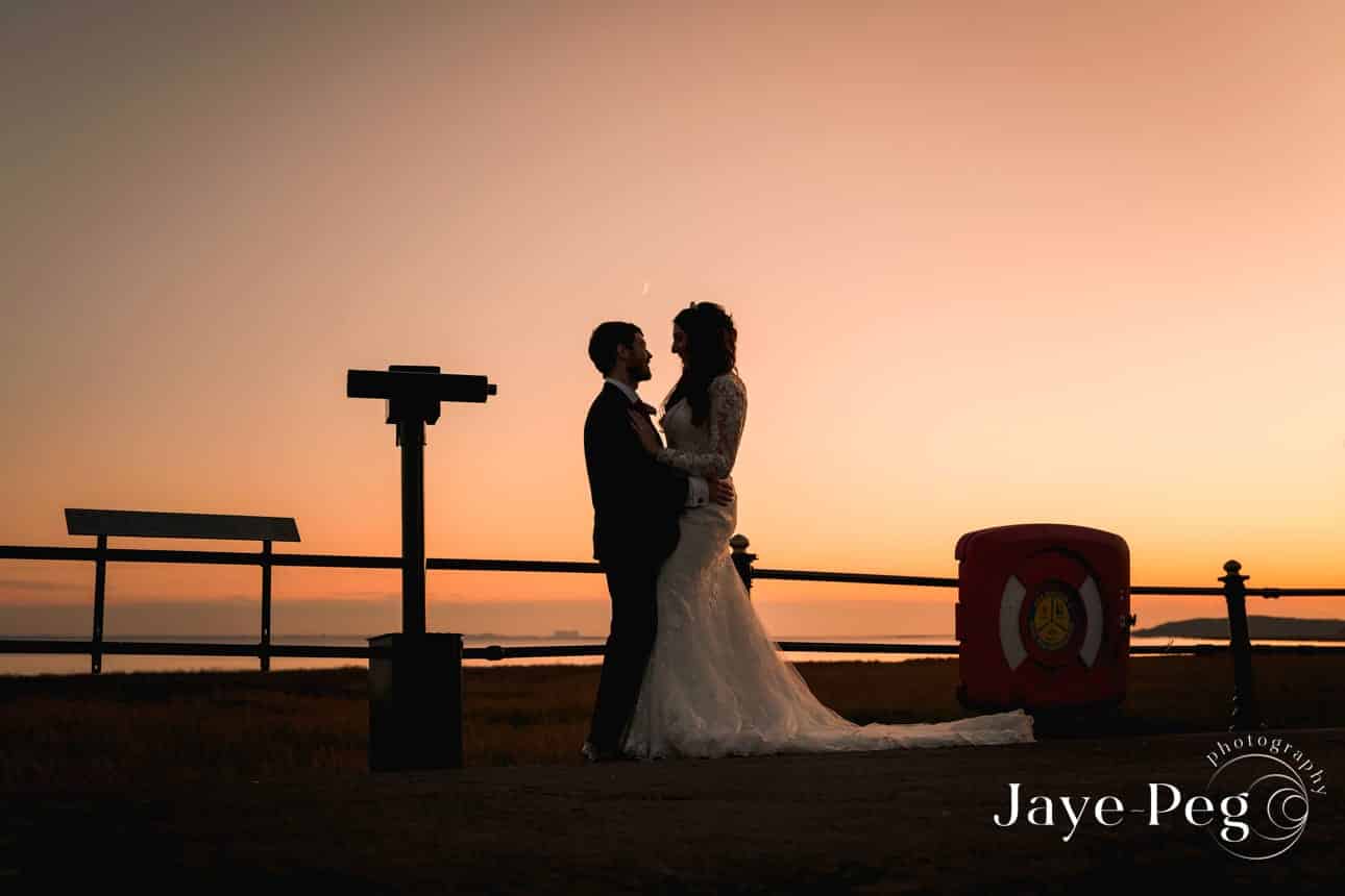 a silhouette of a bride and groom at sunset on the promenade in grange over sands
