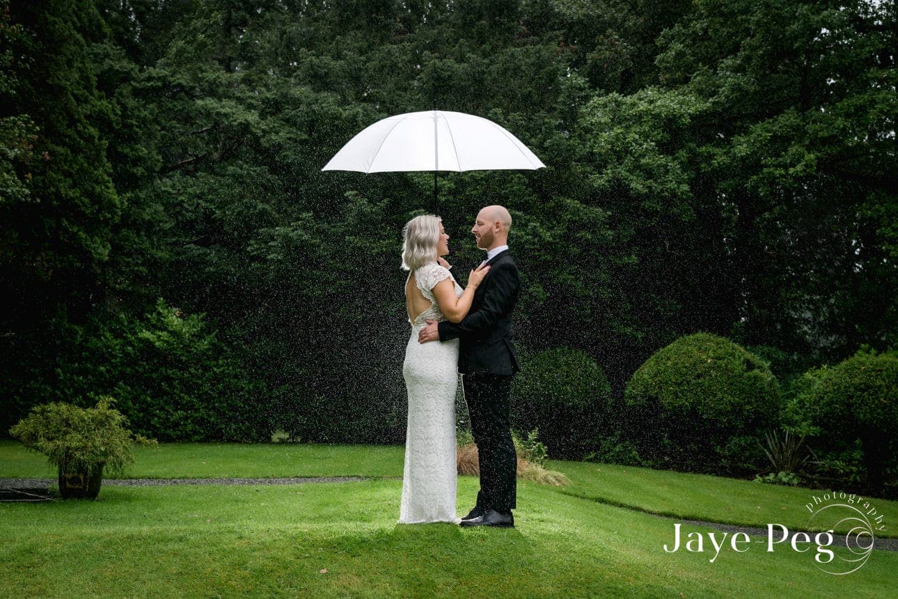 a bride and groom under an umbrella as it rains on their wedding day at briery wood country house hotel