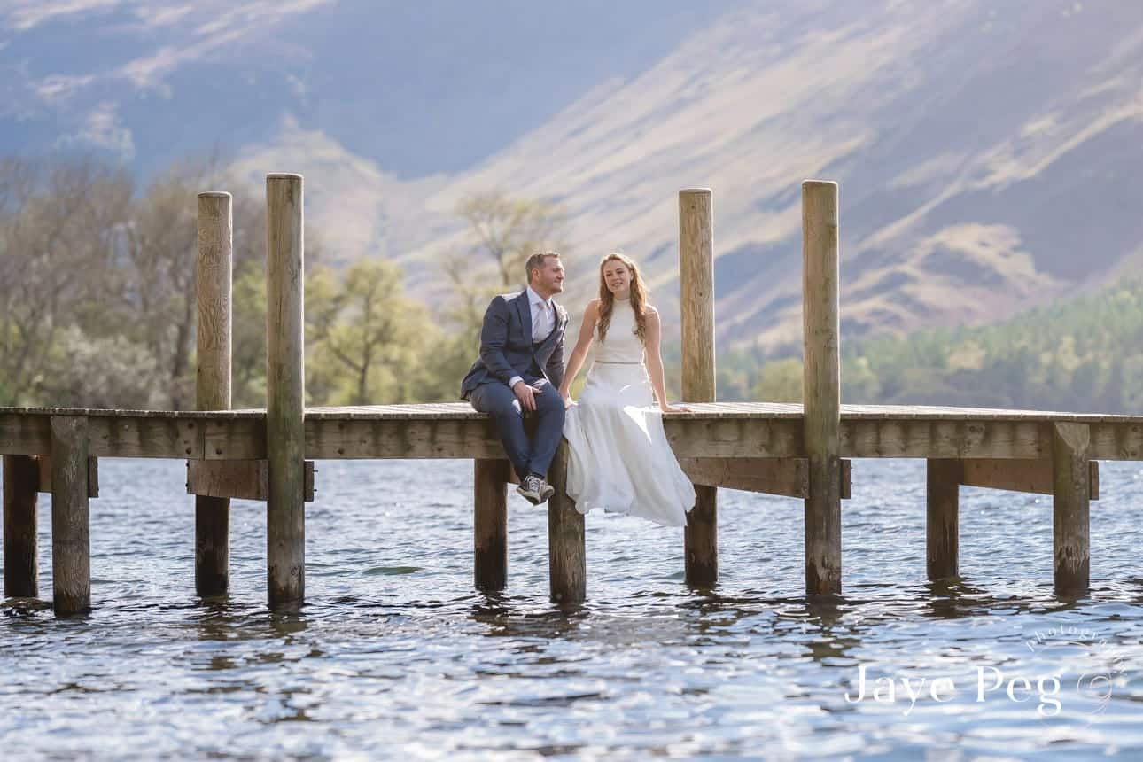 a bride and groom sitting on ashness jetty over derwentwater in the sunshine