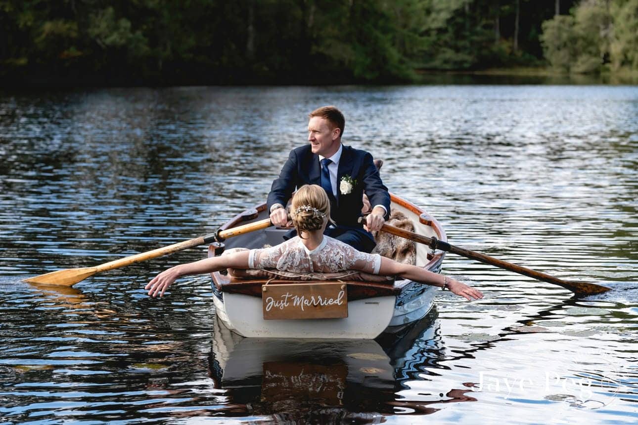 a bride and groom in a rowing boat on knipe tarn at gilpin lake house in the lake district