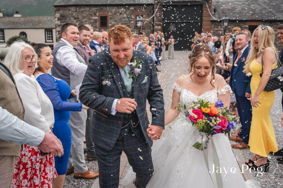 a bride and groom walk past guests throwing confetti at new house farm