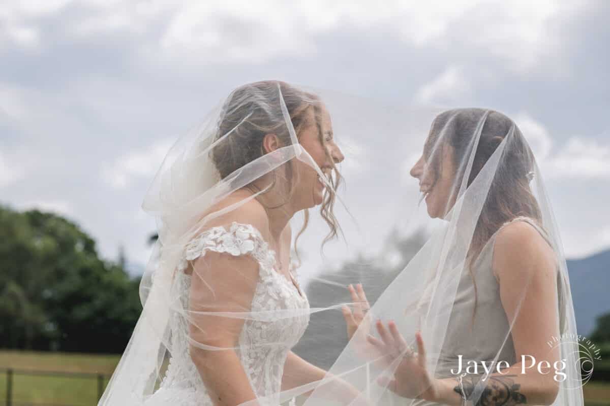 a bride and her maid of honour laughing underneath he wedding veil