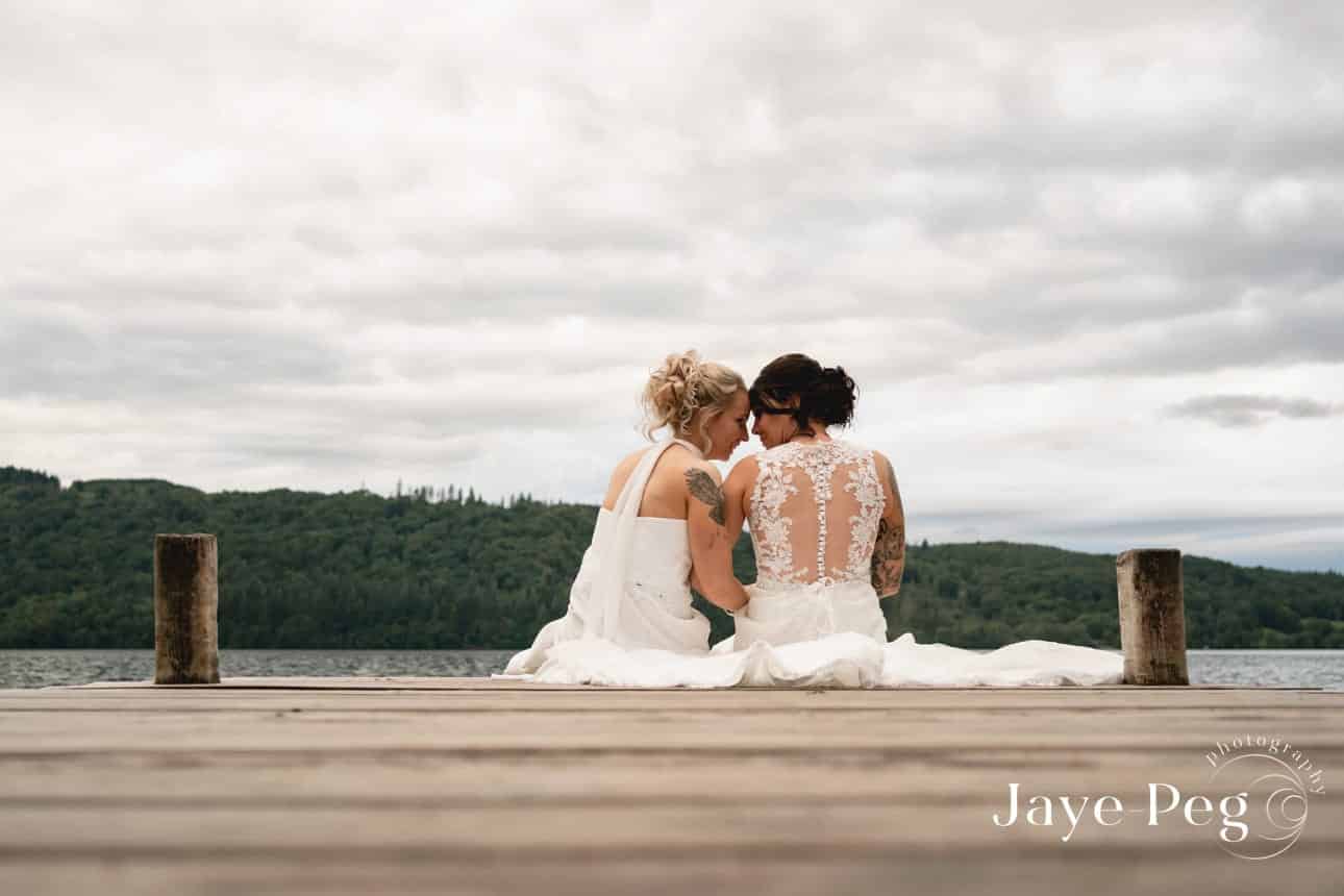 two brides sharing a tender moment on a jetty at windermere