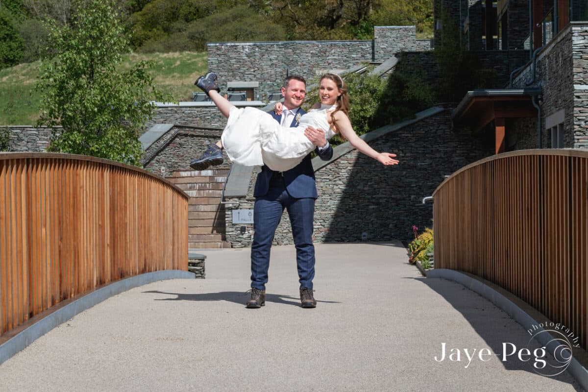 Groom carrying bride on wedding day outdoors.