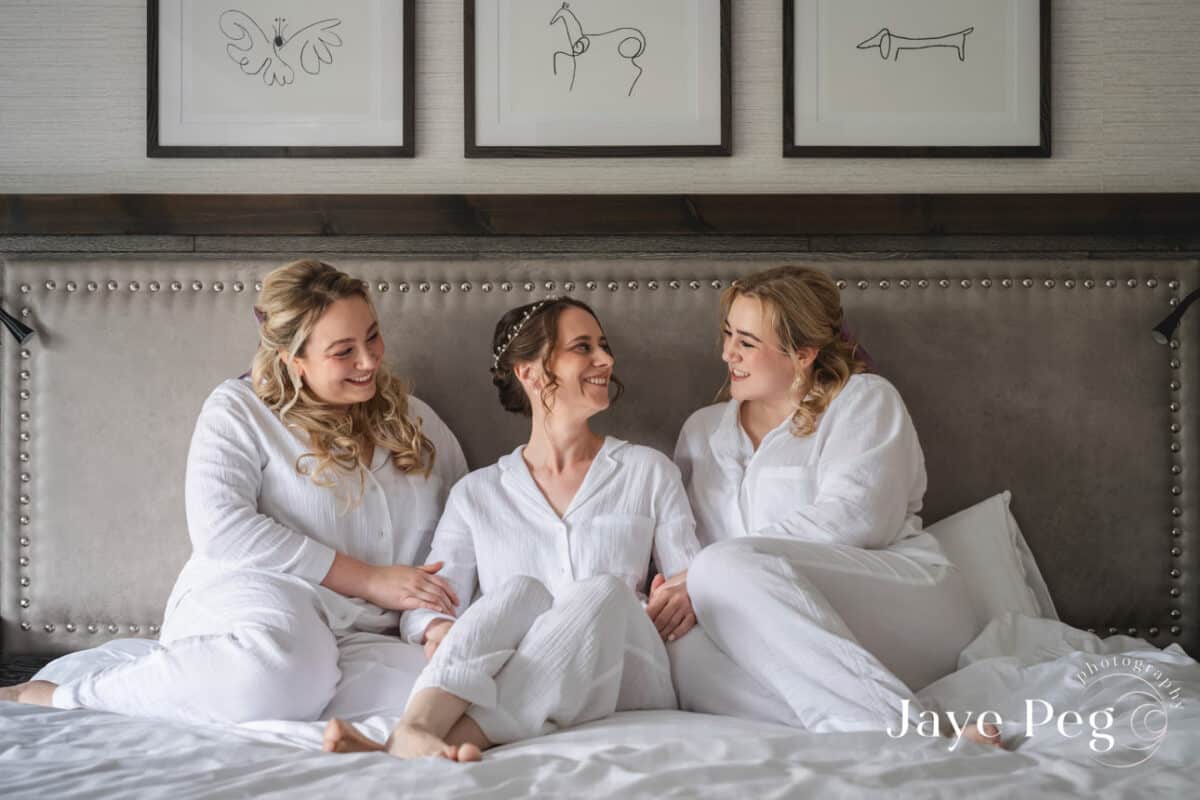 Three women laughing together on bed, cozy atmosphere.