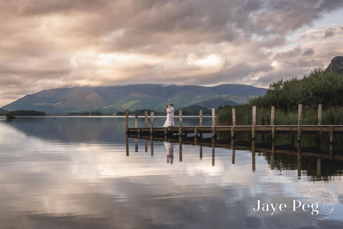 Couple on jetty overlooking tranquil mountain lake at dusk.