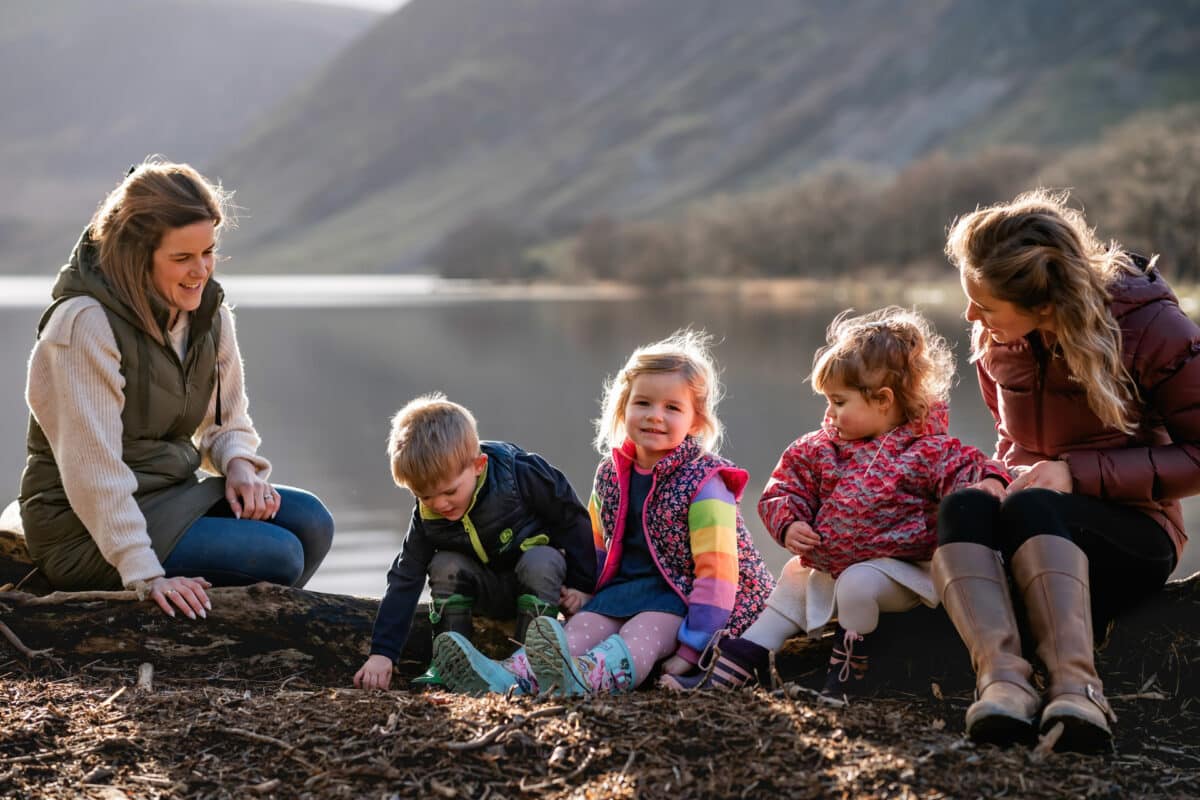 two mums and their young children sitting down with crummock water behind them