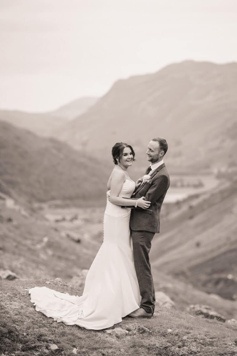 a bride and groom laughing while they share a tender moment on a mountain pass with the valley below behind them