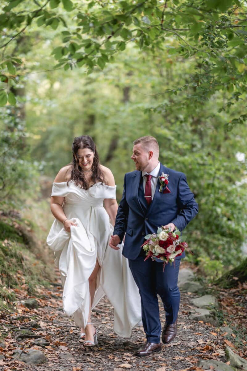a bride and groom walking through woodland