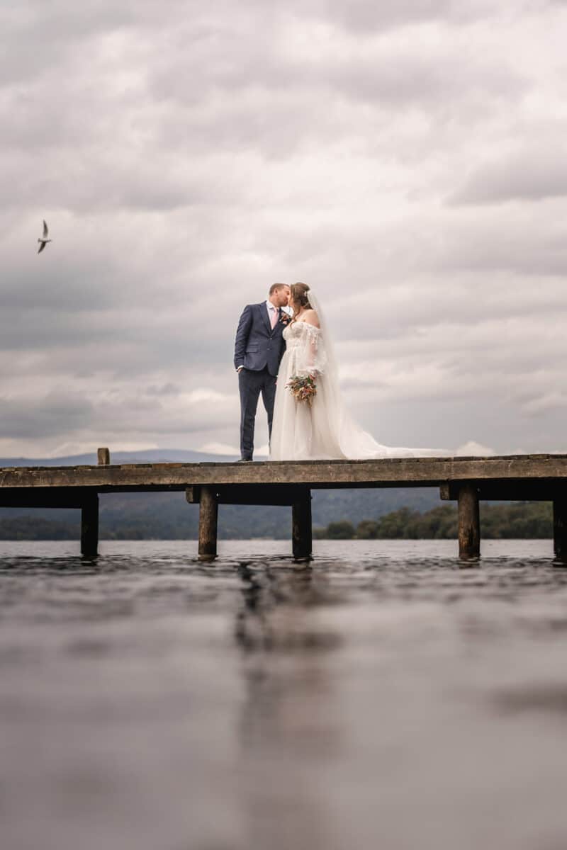a bride and groom embracing on a jetty