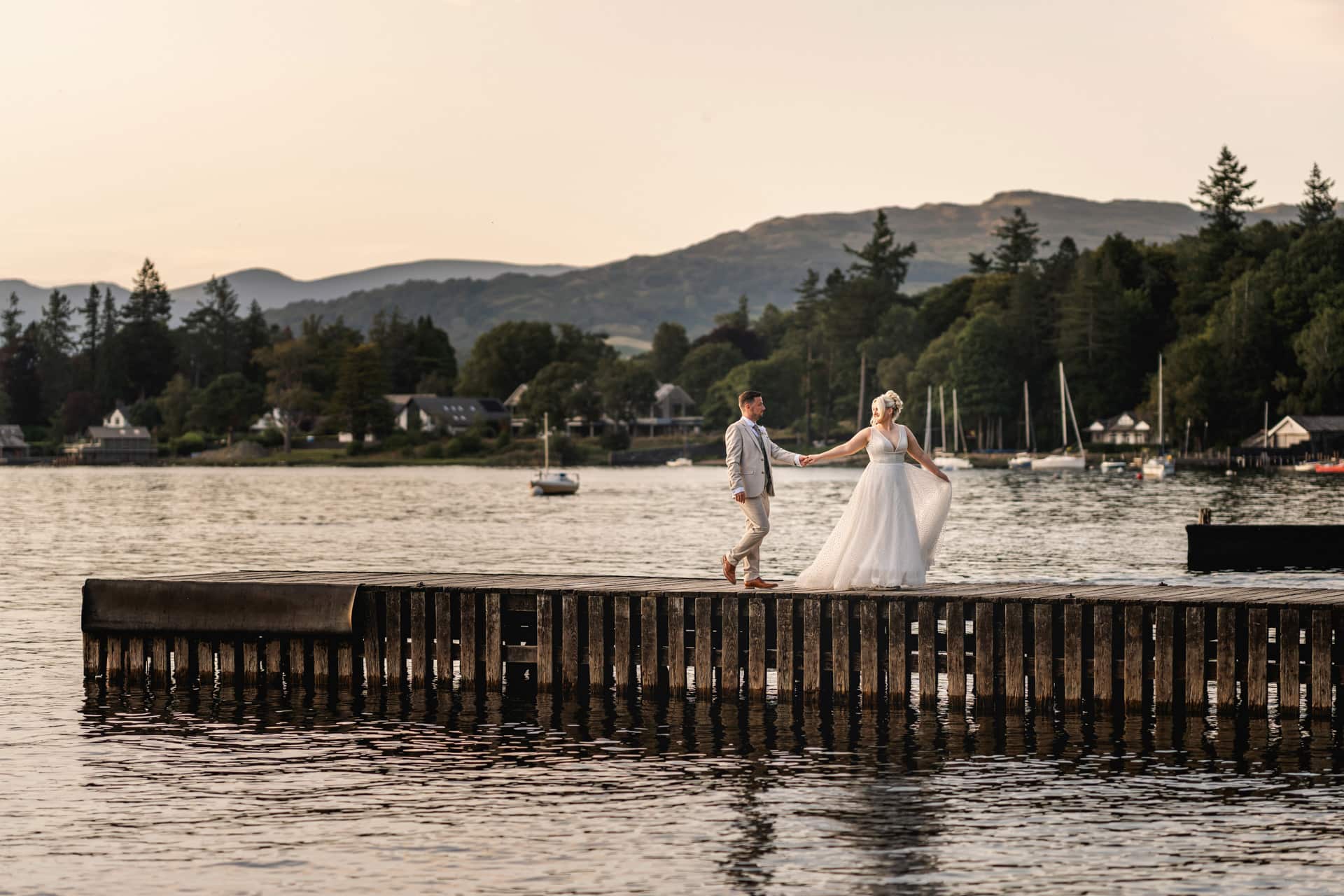 Ben and Leanne walk hand in hand on a Windermere jetty after their Broadoaks Country House wedding
