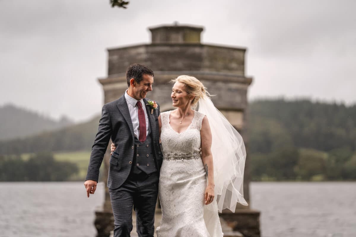 a bride and groom in front of the temple of heroes at storrs hall near windermere