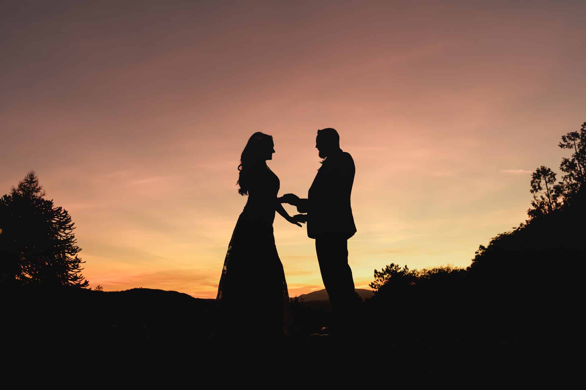 a silhouette of a bride and groom against a sunset sky