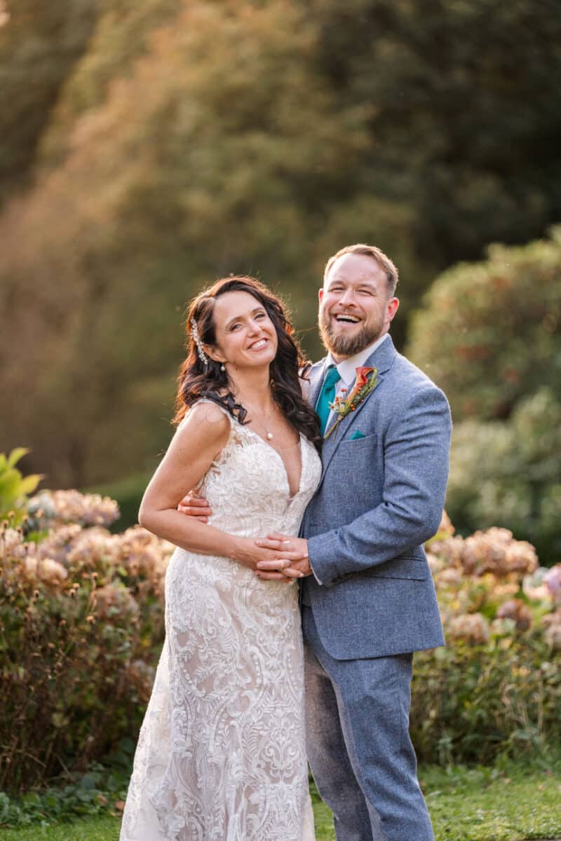 a bride and groom laughing and smiling in a landscaped garden at golden hour