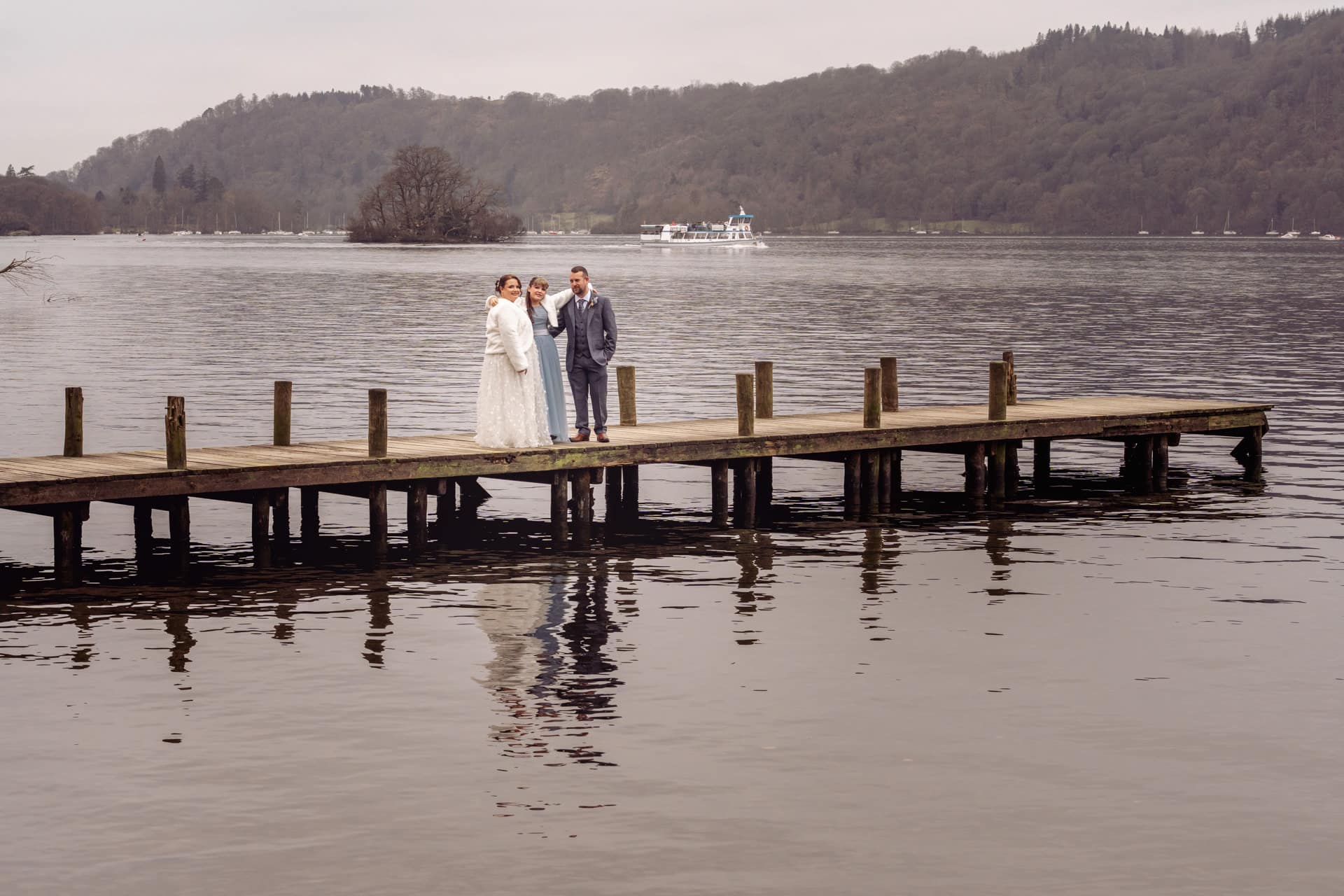 a bride and groom with their daughter on a jetty over windermere