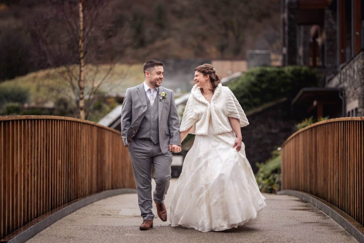 a bride and groom walking over a bridge at lodore falls hotel and spa
